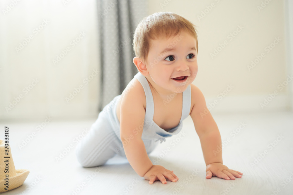 Adorable little baby in gray bodysuit smiling while crawling on floor in cozy room at home Adorable little baby in gray bodysuit smiling while crawling on floor in cozy room at home