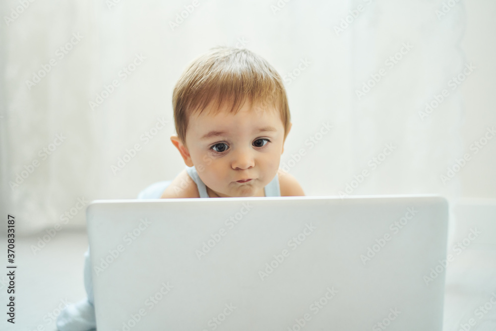 Little toddler sitting on floor and using laptop while playing alone in light room at home Little toddler sitting on floor and using laptop while playing alone in light room at home