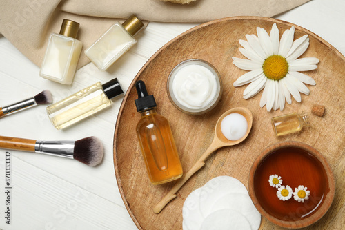 Flat lay composition with chamomile and cosmetic products on white wooden table