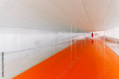 Back view of unrecognizable female standing on shiny orange floor of passage in modern building