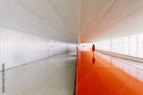 Back view of unrecognizable female standing on shiny orange floor of passage in modern building