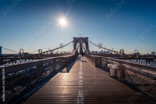 Fotografie Famous Brooklyn bridge over river against clear blue sky with bright sun in New