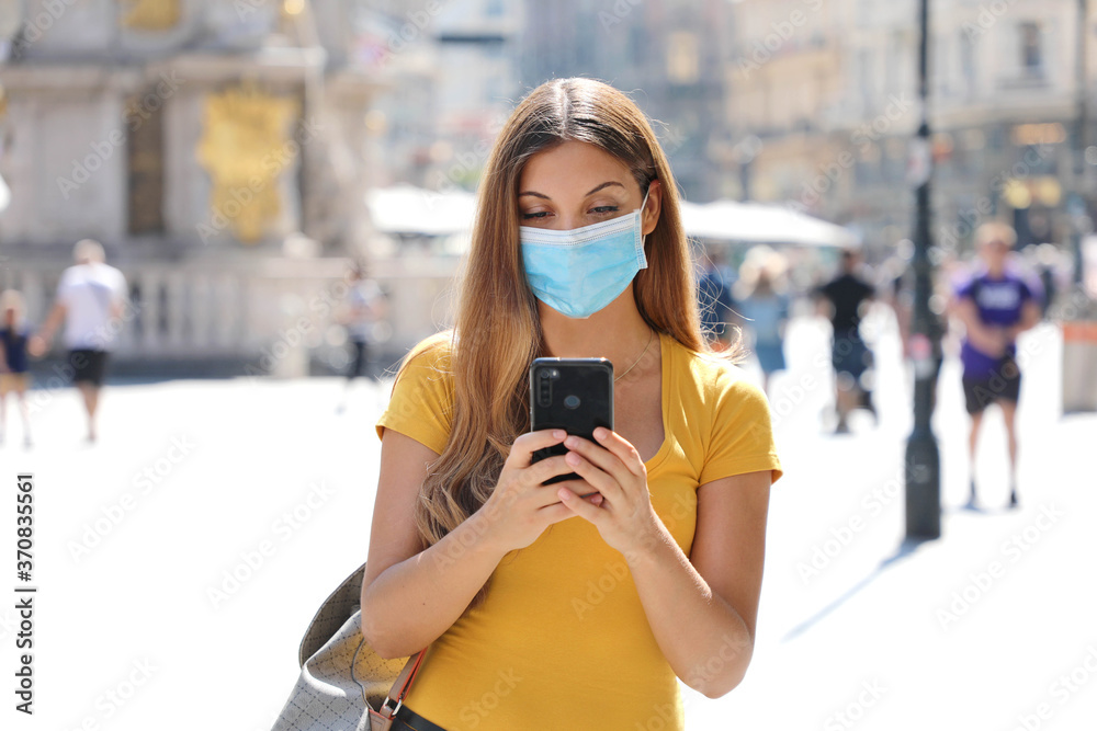 Travel concept. Beautiful young traveler woman with protective mask using application map on smart phone. Tourist girl exploring city with mobile phone.