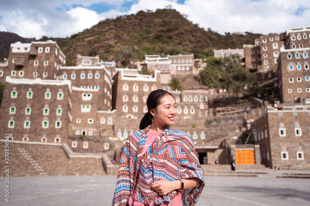 Female tourist standing on background of stone buildings with colorful windows while traveling around Rijal Almaa village in Saudi Arabia Female tourist standing on background of stone buildings with colorful windows while traveling around Rijal Almaa village in Saudi Arabia