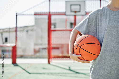 Crop of young sportswoman with basketball ball while standing on court in sunny summer day photo