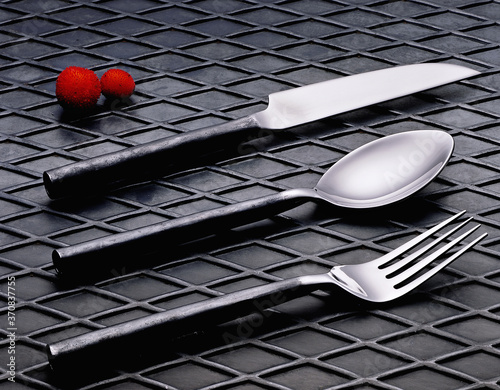 Metal spoon placed on black textured table between knife and fork