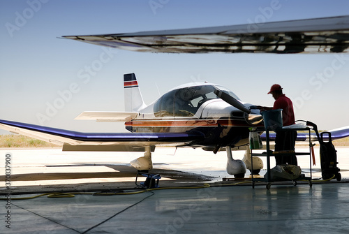 Side view of male employee in uniform cleaning jet airplane while standing on airfield during sunny day