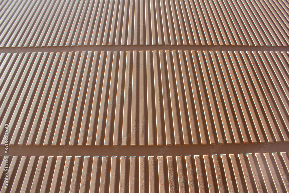 Surface of the wall with a decorative light beige plaster. Textured concrete wall with vertical lines and stripes as a texture or background. Surface of the wall with a decorative light beige plaster. Textured concrete wall with vertical lines and stripes as a texture or background.