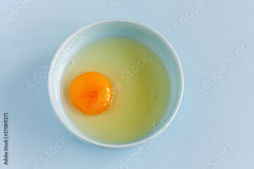 Fresh organic raw yolk and white of egg in light blue bowl on pastel background. Healthy breakfast and fresh ingredients. Selective focus. Top view. Space for text.