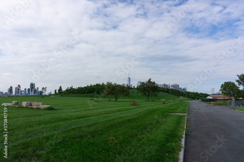 Lawn with trees, benches and view of Manhattan in the background. Park in the Governors Island