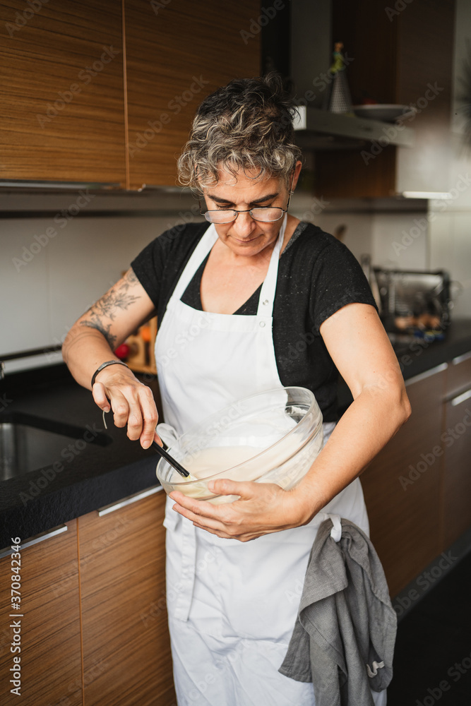 Side view of concentrated housewife in apron mixing ingredients in bowl and preparing pastry Side view of concentrated housewife in apron mixing ingredients in bowl and preparing pastry