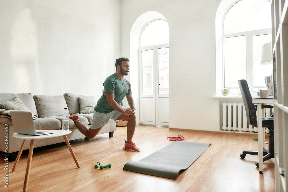 Get Fit Online. Full length shot of young active man watching online video training on laptop, exercising during morning workout at home. Sport, healthy lifestyle Get Fit Online. Full length shot of young active man watching online video training on laptop, exercising during morning workout at home. Sport, healthy lifestyle