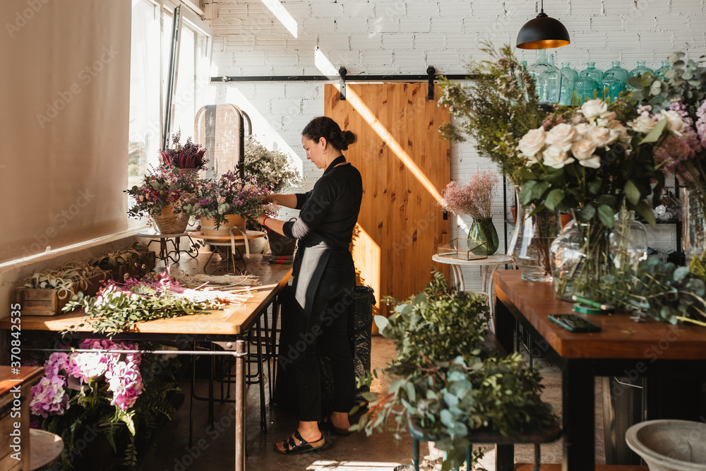 Side view of concentrated female designer arranging decorative blooming bouquets while working on order for event in creative floristry studio Side view of concentrated female designer arranging decorative blooming bouquets while working on order for event in creative floristry studio