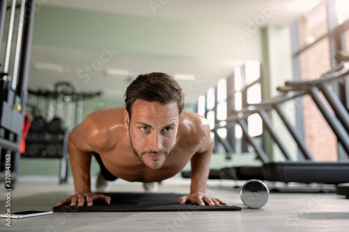 Muscular build athlete exercising push-up at health club.