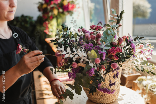 Crop of side view of concentrated female designer arranging decorative blooming bouquets while working on order for event in creative floristry studio