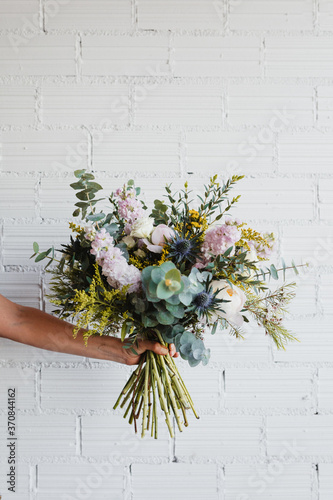 Crop anonymous female holding beautiful blooming bouquet of various fresh flowers and decorative plants against white brick wall photo