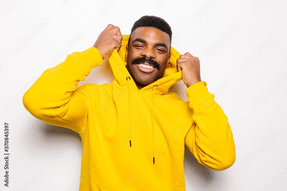 Cheerful black man over white plain background. He is looking at camera and smiling wearing a yellow hoodie Cheerful black man over white plain background. He is looking at camera and smiling wearing a yellow hoodie