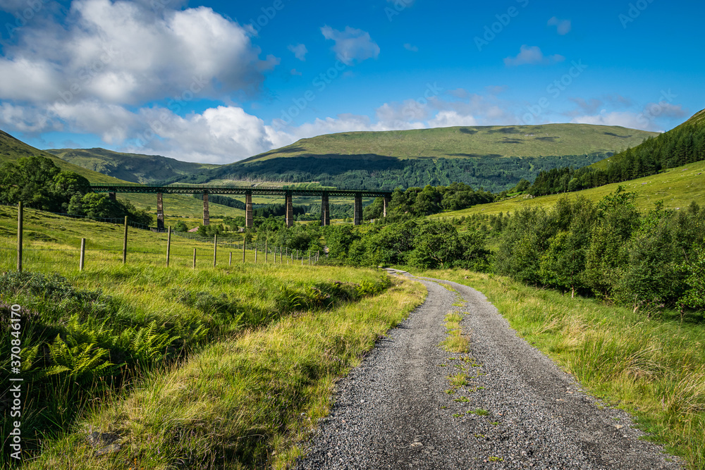 Road up Glen Auch in Scottish Highlands with train viaduct on the horizon. Beautiful summer Scottish landscape. Road up Glen Auch in Scottish Highlands with train viaduct on the horizon. Beautiful summer Scottish landscape.