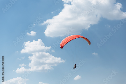 Blue Paraglider flying into the sky with clouds in a sunny day