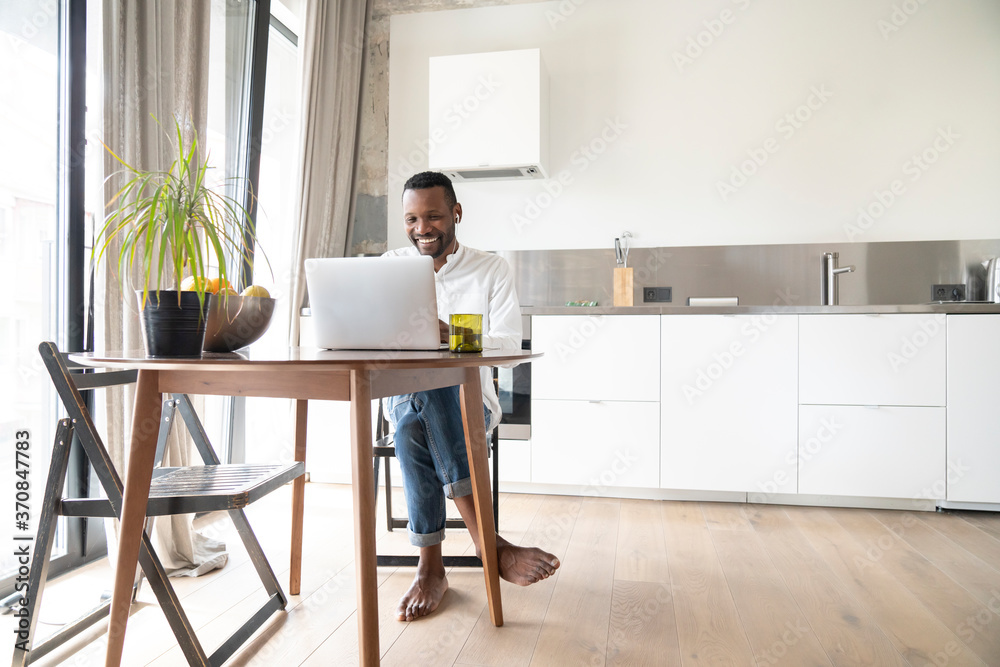 Portrait of smiling man sitting at table in modern apartment using laptop and earphones Portrait of smiling man sitting at table in modern apartment using laptop and earphones