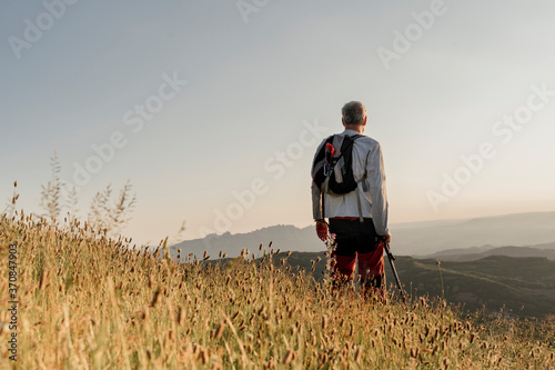 Retired senior man standing by cattail plants while looking at landscape during sunset