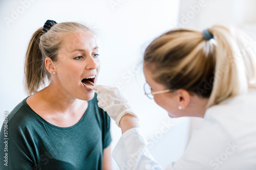 Female doctor examining female patient with tongue depressor
