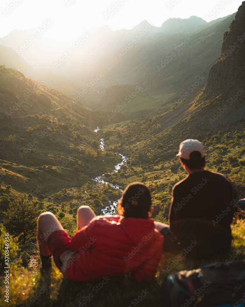Two young men sitting on the grass watching the sunset on top of a valley in Pyrenees