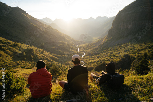 Group of young men sitting on the grass watching the sunset on top of a valley in Pyrenees