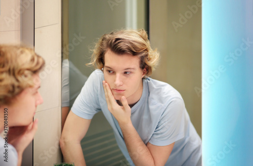 young man looking in the mirror,combing his hair,looking at problems on face