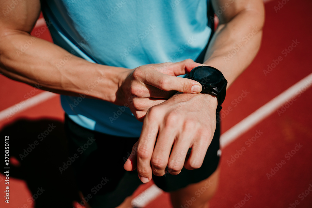 Male athlete on tartan track checking smartwatch