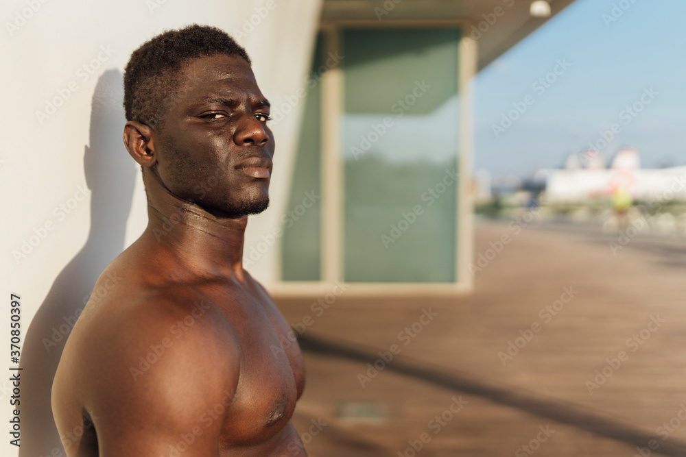 Shirtless man standing against wall on sunny day Shirtless man standing against wall on sunny day