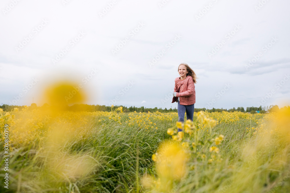 Smiling girl in pink coat running by rape field Smiling girl in pink coat running by rape field