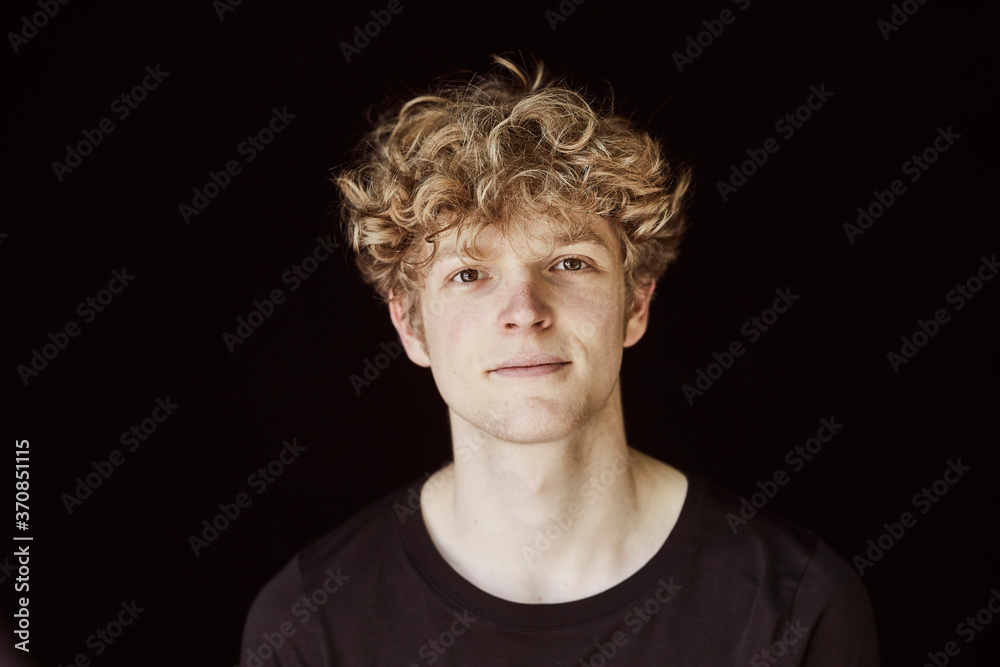 Portrait of young man with curly blond hair against black background Portrait of young man with curly blond hair against black background