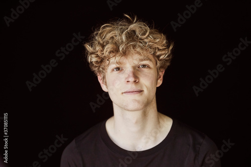 Portrait of young man with curly blond hair against black background
