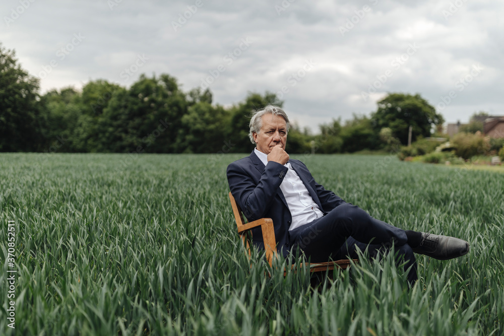Senior businessman sitting on a chair in a field in the countryside Senior businessman sitting on a chair in a field in the countryside