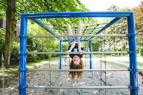 Smiling girl hanging upside down on jungle gym in playground at park