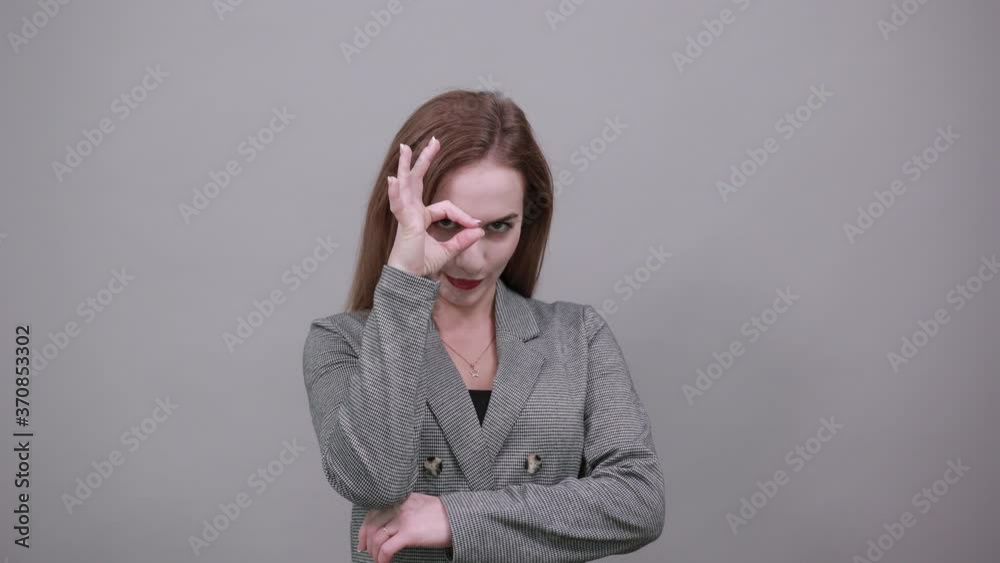View of hand fingers showing ok sign, gesturing making okay, human emotions, facial expressions, feelings. Young attractive woman, dressed gray jacket, with green eyes, light brown hair, background View of hand fingers showing ok sign, gesturing making okay, human emotions, facial expressions, feelings. Young attractive woman, dressed gray jacket, with green eyes, light brown hair, background