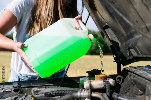 Midsection of woman on road trip pouring coolant in engine during sunny day