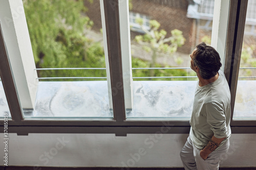 Senior man looking out of window in a loft flat