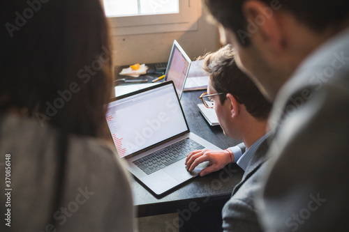 Three business people sharing laptop at desk in office