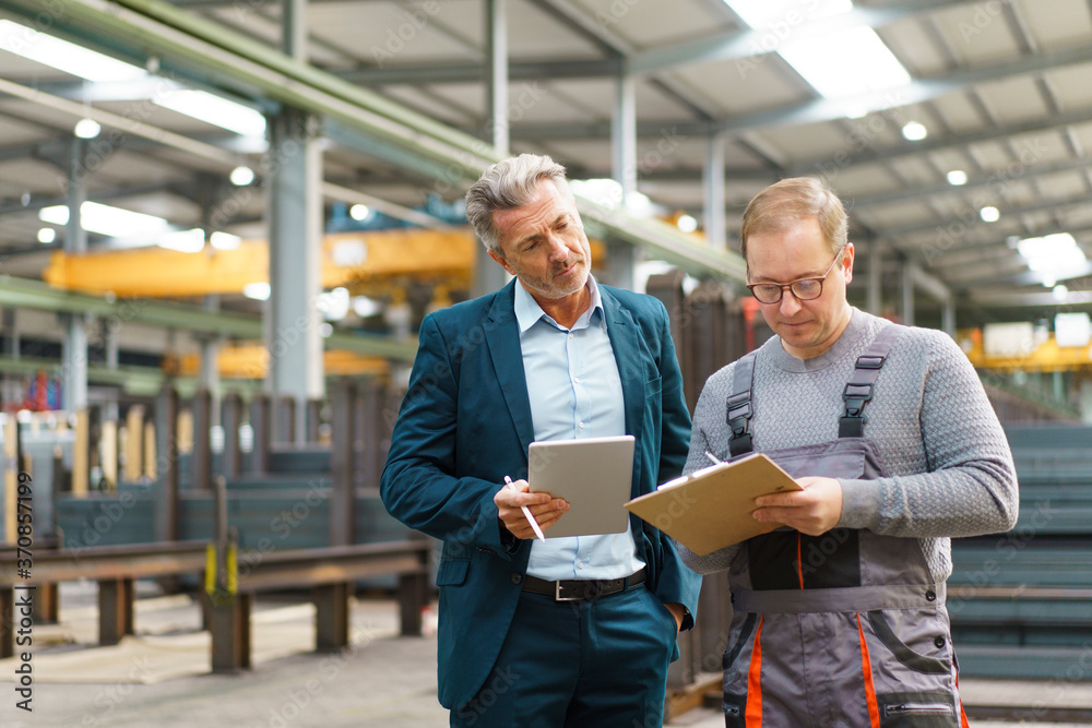 Businessman with tablet and employee with clipboard in a factory Businessman with tablet and employee with clipboard in a factory