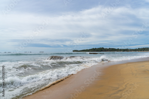 Tropical beach with rocks in the sea. palm trees on the background. cloudy sky. Arugam bay, Sri Lanka