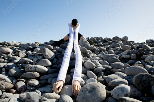 Woman with artificial long hands sitting on pebbles against clear sky photo