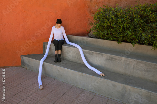 Woman with long artificial hands sitting on concrete steps by plants