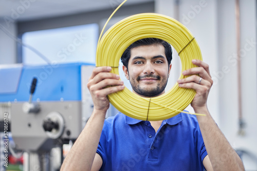 Confident male worker looking through rolled up cables in factory photo