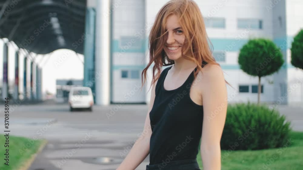 Beautiful smiling red-haired woman walks on street at sunset. Portrait of young female on the street Beautiful smiling red-haired woman walks on street at sunset. Portrait of young female on the street