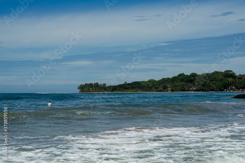 Surfer on the sea, palm trees on the background, blue sky. Arugam Bay, Sri Lanka. 