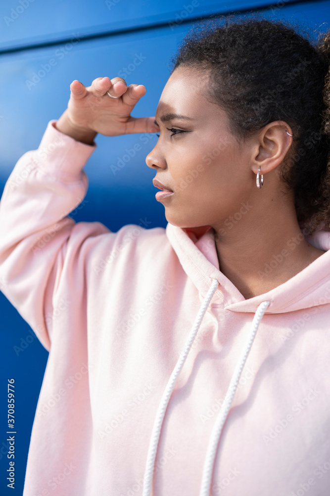 Young woman looking out wearing pink hoodie sweater in front of blue wall Young woman looking out wearing pink hoodie sweater in front of blue wall