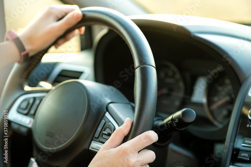 Close up view of woman hands holding steering wheel driving a car on city street on sunny day. © bilanol