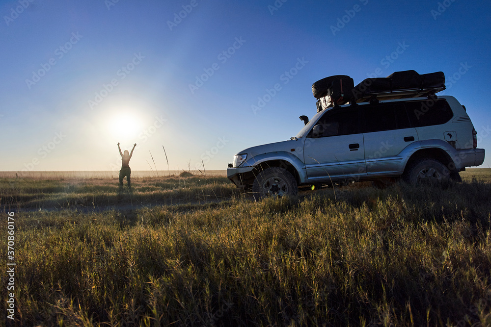 Woman standing with arms raised by off-road vehicle at Makgadikgadi Pans, Botswana Woman standing with arms raised by off-road vehicle at Makgadikgadi Pans, Botswana